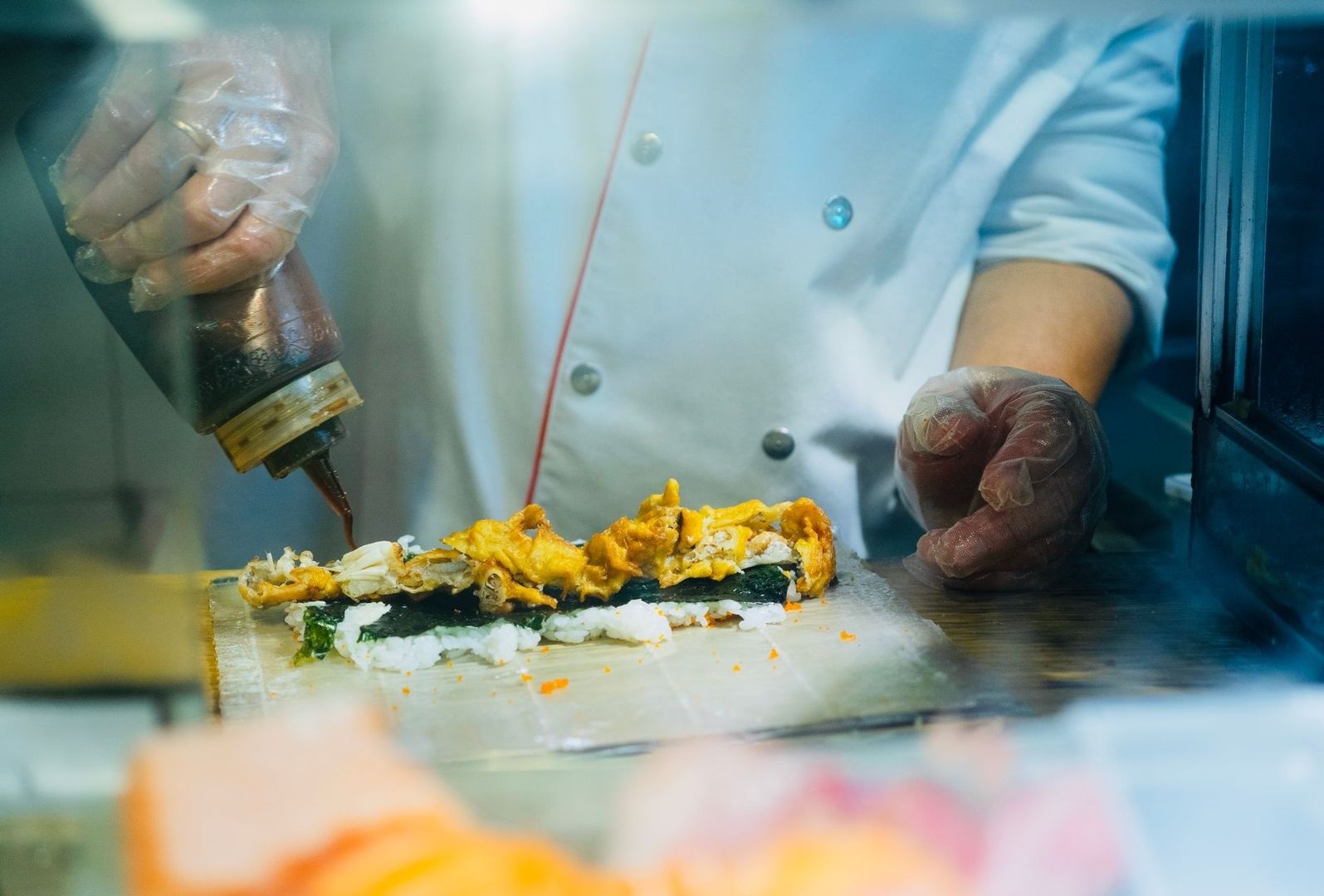 Chef in handschoenen brengt saus aan op een gerecht met rijst