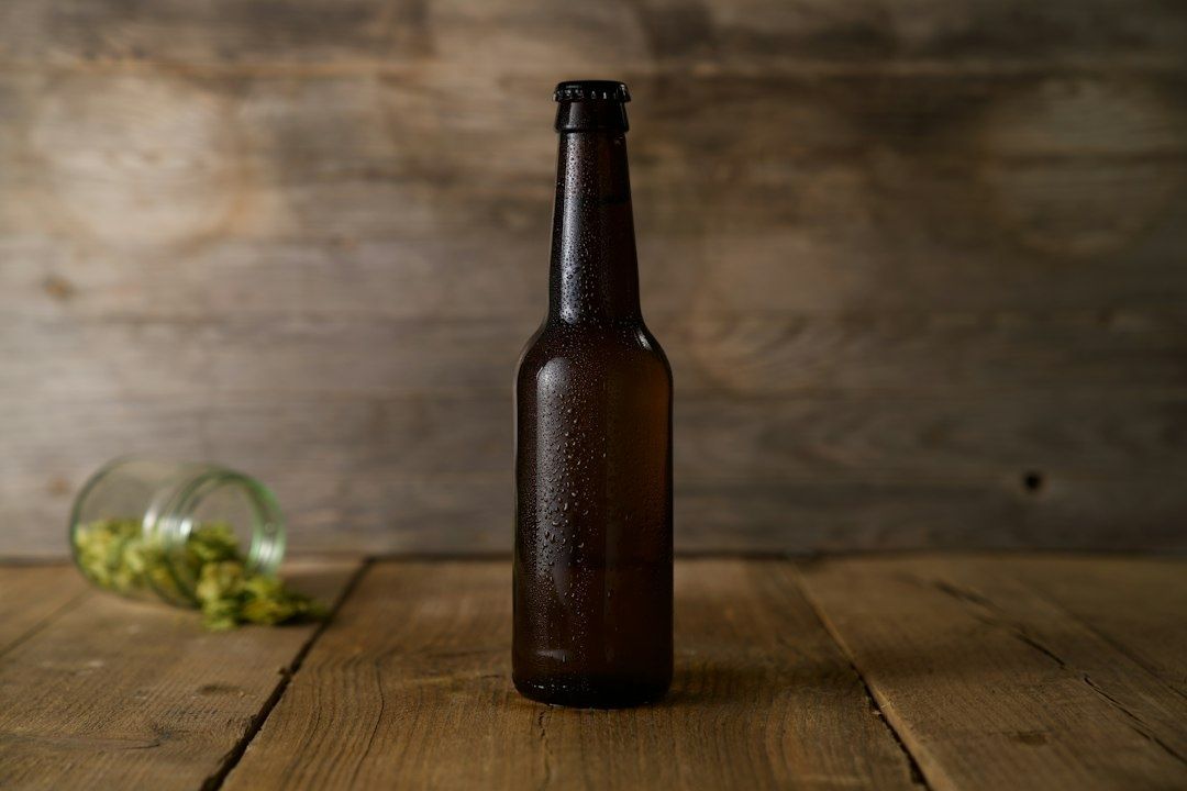 Donkere ciderfles op een houten tafel naast gemorste hopbellen